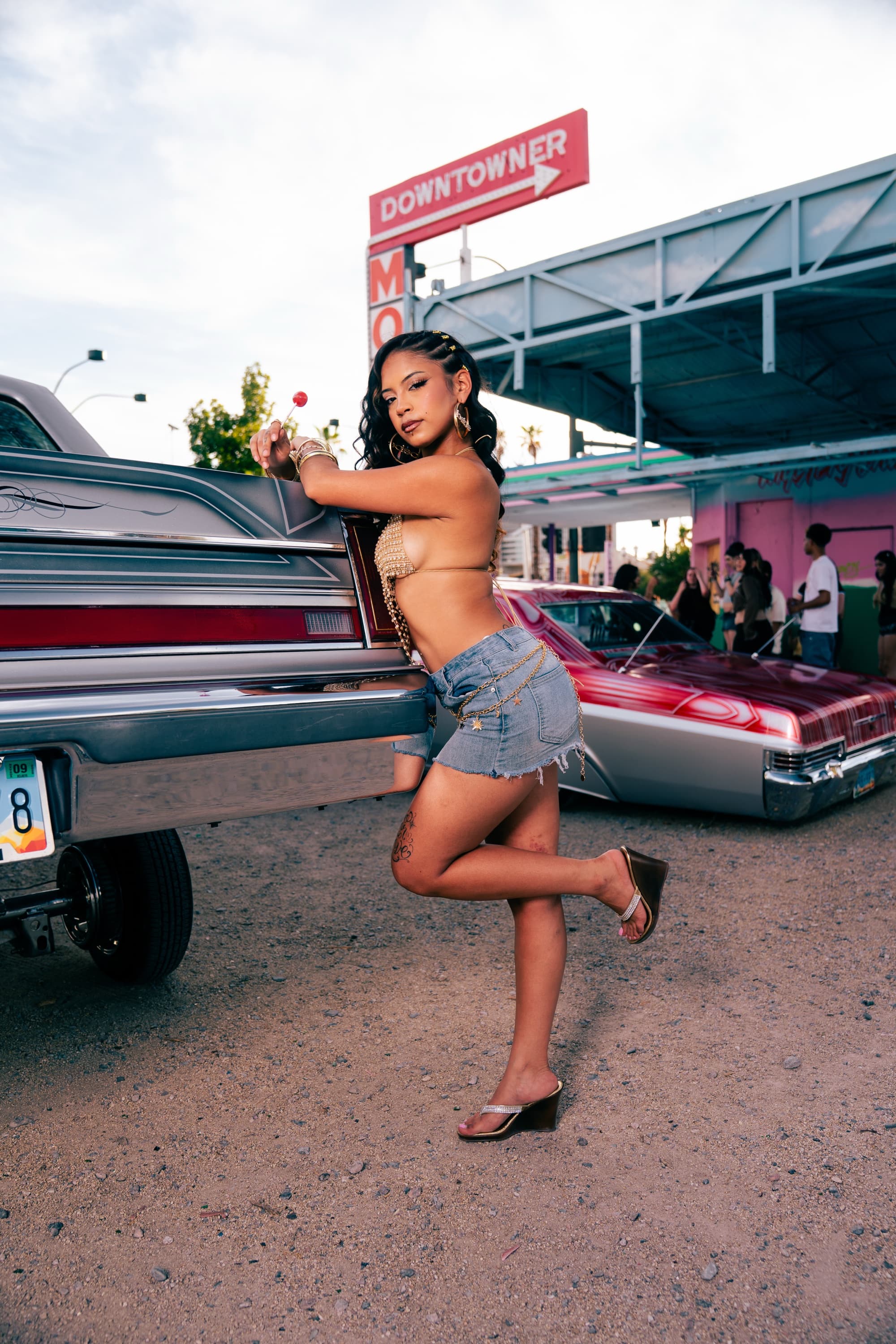 Model posing on a silver Lincoln lowrider under the Downtowner Motel sign in downtown Las Vegas