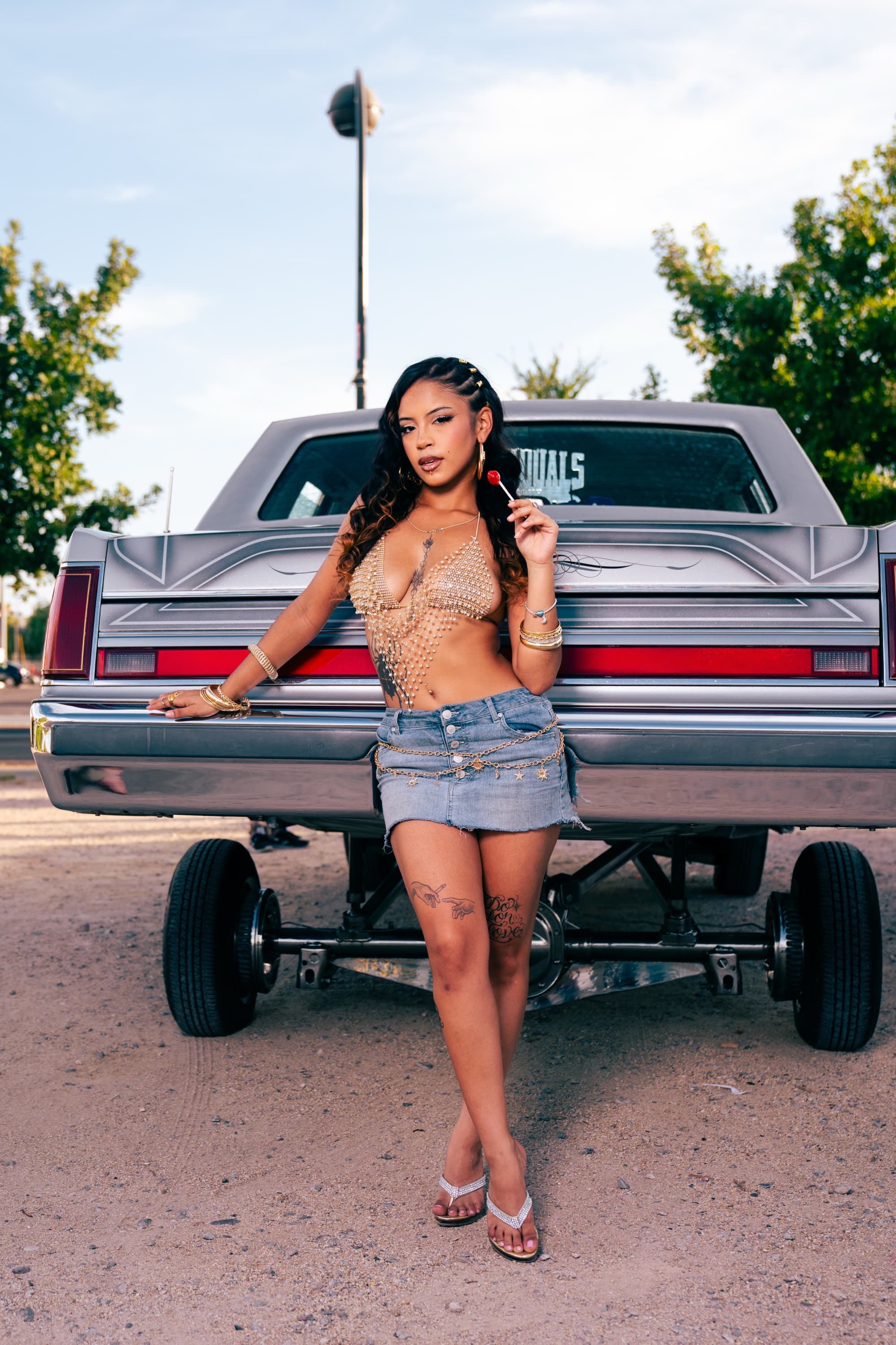 Model leaning on the rear of a locked-up silver Lincoln lowrider with hydraulics at golden hour