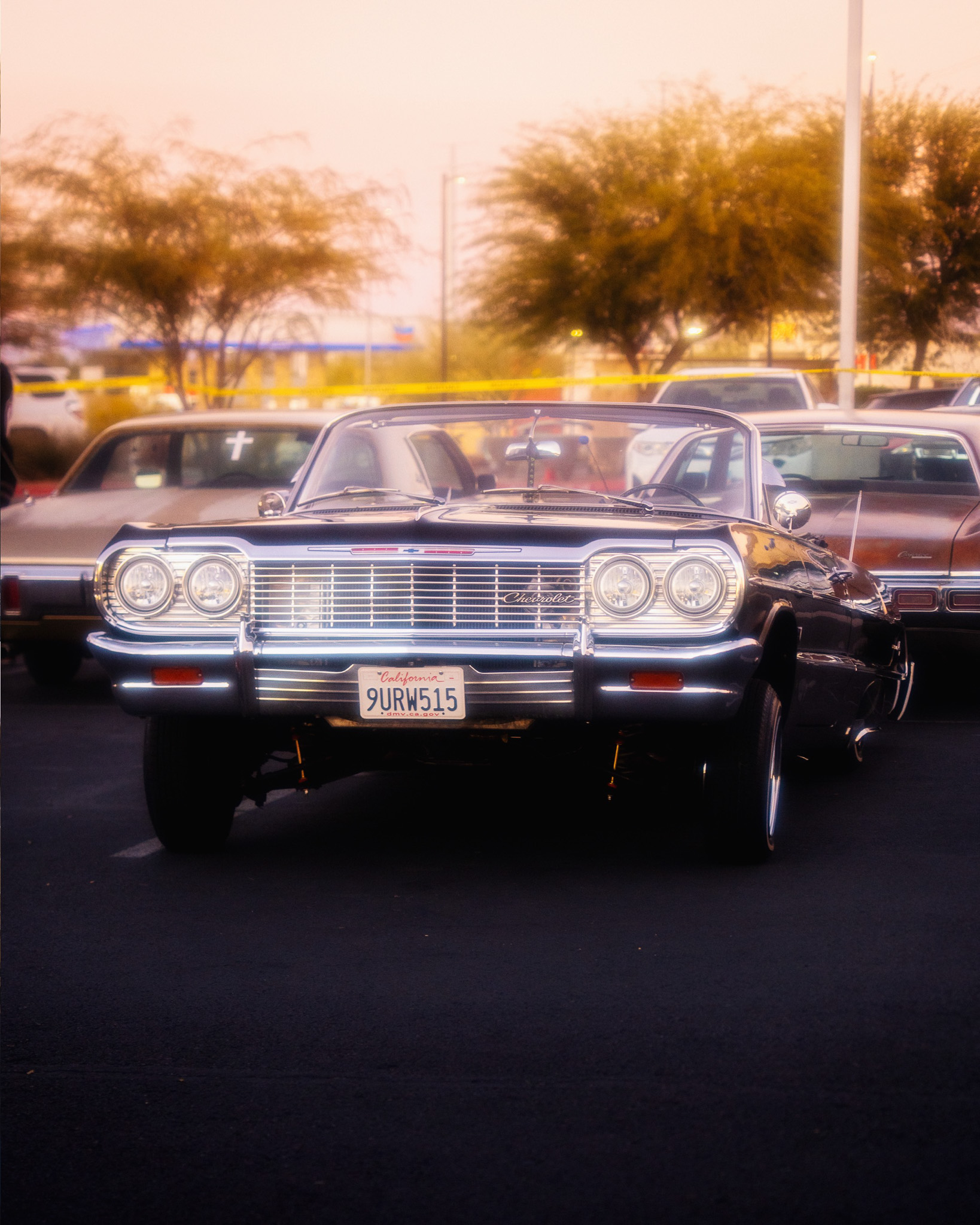 Black 1964 Chevrolet Impala lowrider at golden hour car show with chrome grille
